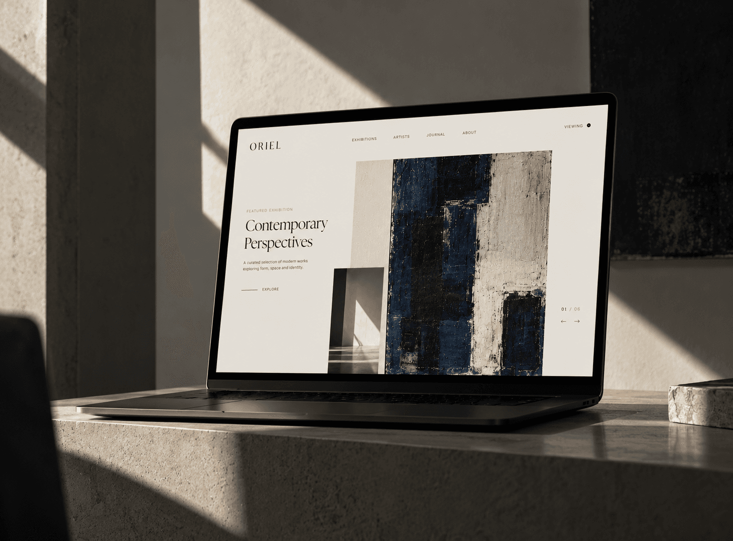 Laptop showing the Oriel Gallery website with its Contemporary Perspectives exhibition, on a stone desk in soft afternoon light